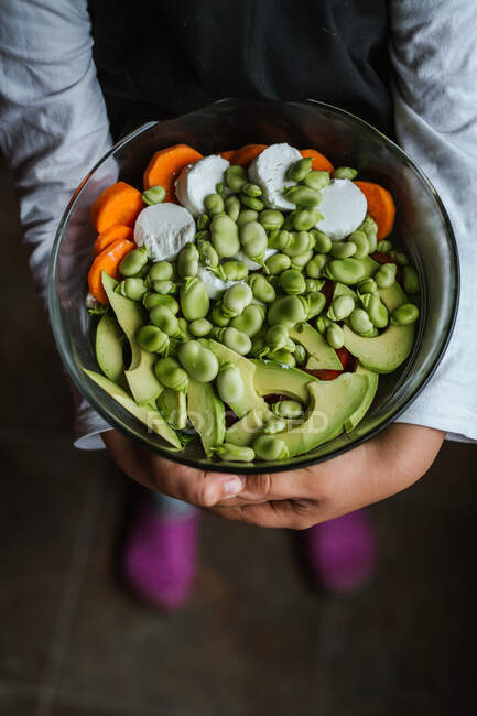 Hands of anonymous little girl holding bowl of healthy vegetable salad while standing in kitchen at home — Stock Photo