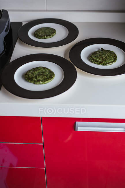 Placas com costeletas vegetarianas verdes na bancada na cozinha em casa — Fotografia de Stock