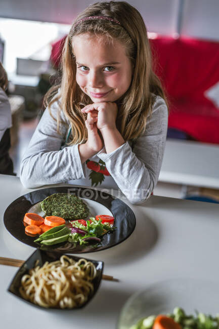 Menina esperando para comer macarrão saboroso com costeletas vegetarianas e legumes enquanto sentado à mesa em casa — Fotografia de Stock