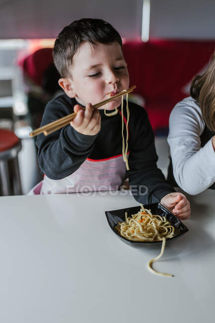 Menino e menina comendo macarrão saboroso com costeletas vegetarianas e legumes enquanto se senta à mesa em casa — Fotografia de Stock