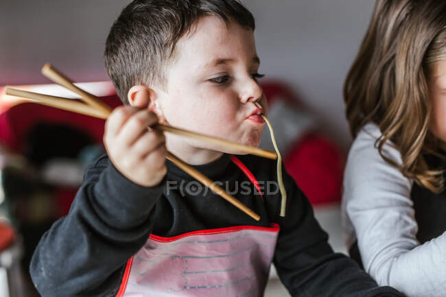Menino comendo macarrão saboroso enquanto sentado à mesa em casa — Fotografia de Stock