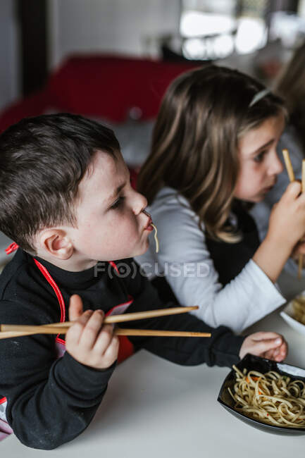Boy and girl eating tasty noodles with vegetarian cutlets and vegetables while sitting at table at home — Stock Photo