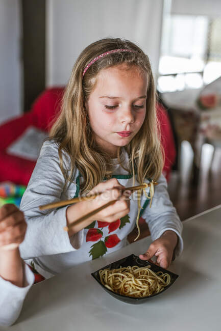 Menina comendo macarrão saboroso com costeletas vegetarianas e legumes enquanto sentado à mesa em casa — Fotografia de Stock