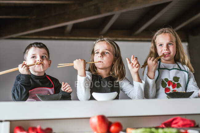 Garçon et deux filles manger des nouilles savoureuses avec des escalopes végétariennes et des légumes tout en étant assis à la table à la maison — Photo de stock