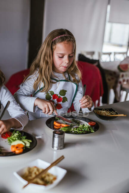 Chicas disfrutando de sabrosos fideos con chuletas vegetarianas y verduras mientras están sentadas en la mesa en casa - foto de stock