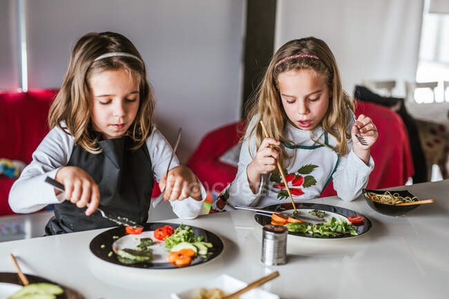 Chicas disfrutando de sabrosos fideos con chuletas vegetarianas y verduras mientras están sentadas en la mesa en casa - foto de stock