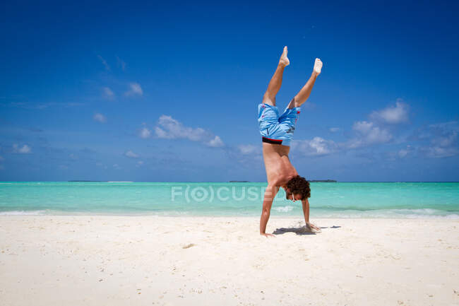 Unrecognizable male standing upside down near turquoise sea — Stock Photo