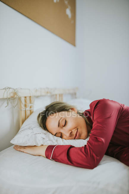 Молода симпатична жінка в піжамі посміхаючись під час сну на ліжку в спальні — стокове фото