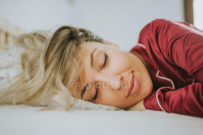 Junge hübsche Frau im Schlafanzug lächelt, während sie im Schlafzimmer auf dem Bett schläft — Stockfoto