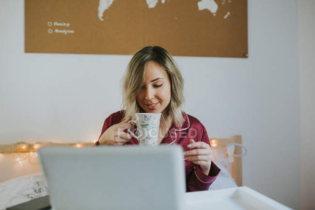 Jovem mulher bonita de pijama sentado na cama com café e tablet digital na bandeja de mesa — Fotografia de Stock