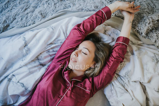 Young pretty woman in pajamas smiling while relaxing on bed — Stock Photo