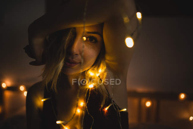 Jovem mulher elegante em roupa interior sentado na cama cercado com guirlanda luz — Fotografia de Stock