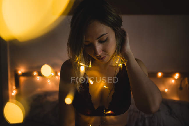 Young sensual woman in underwear sitting in bed surrounded with light garland — Stock Photo