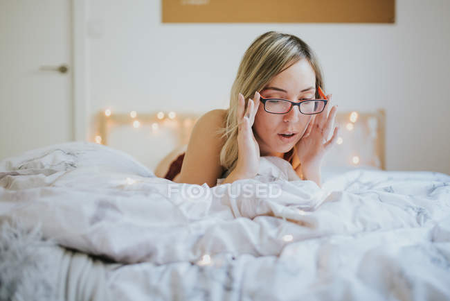 Jovem mulher em óculos e roupa interior deitada na cama de manhã — Fotografia de Stock