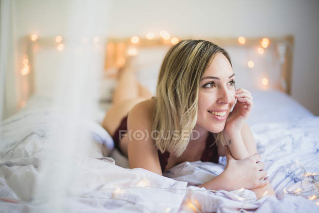 Молода жінка в нижній білизні лежить у ліжку з вогнями — стокове фото