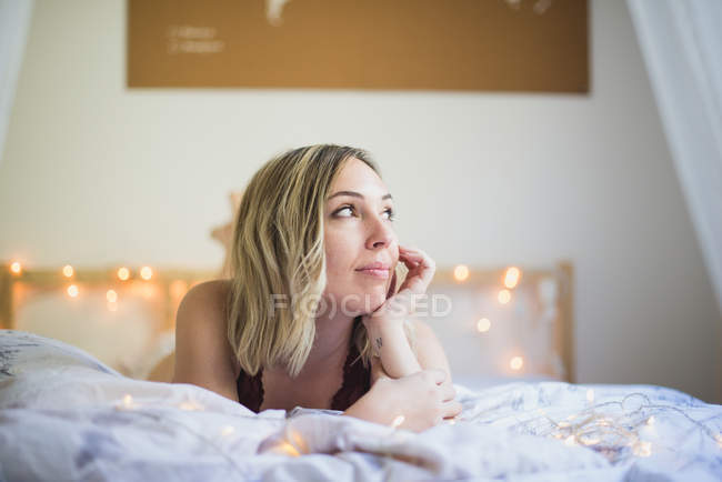 Young woman in underwear lying in bed with lights — Stock Photo