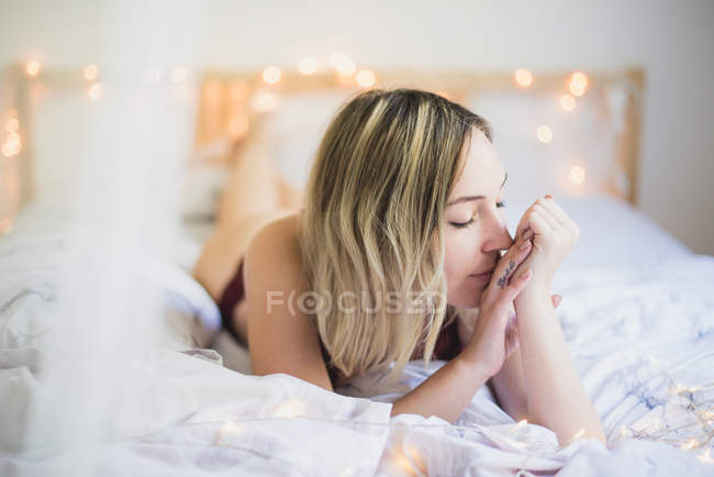 Молодая мечтательная женщина в нижнем белье лежит в постели с огнями — стоковое фото