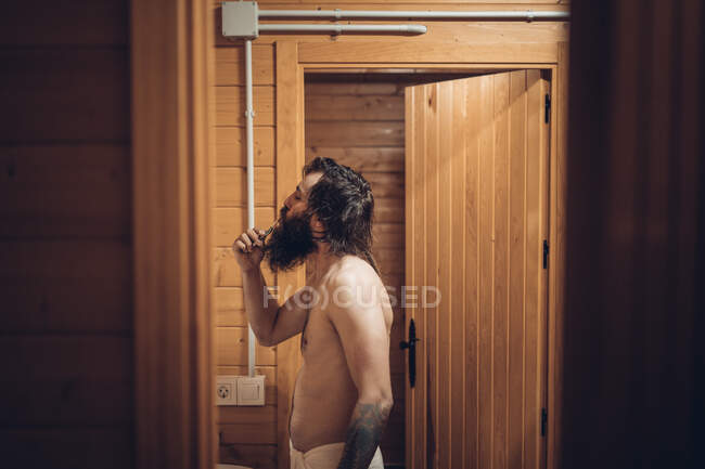 Bearded man brushing teeth in wooden house — Stock Photo