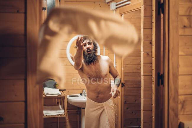 Trendy hipster with naked torso throwing towel after having shower in wooden country house — Stock Photo