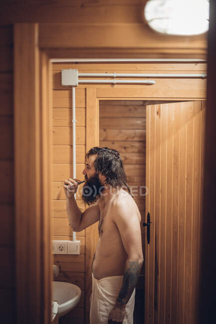 Бородатий чоловік чистить зуби в дерев'яному будинку — стокове фото