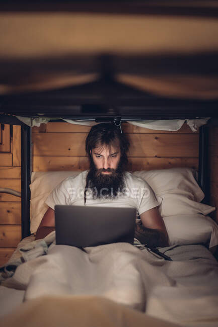Homme utilisant un ordinateur portable dans un lit superposé rustique — Photo de stock