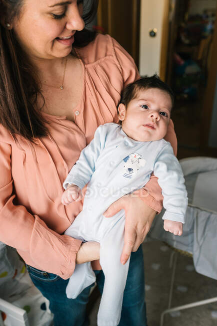 Young mother holding on hands newborn baby while standing at home — Stock Photo