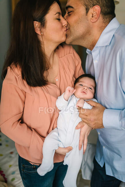 Glückliche junge Mutter hält Neugeborenes in der Hand, während sie den Vater zu Hause küsst — Stockfoto