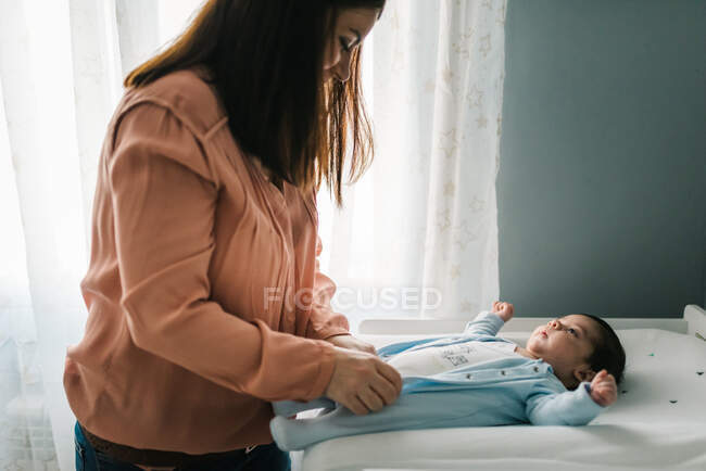Молодая мать одевает новорожденного ребенка на пеленальный стол дома — стоковое фото