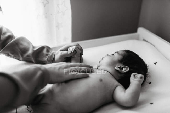 Зверху безлика жінка торкається ніжно голого новонародженого немовляти, лежачи на змінному столі і дивлячись на камеру — стокове фото