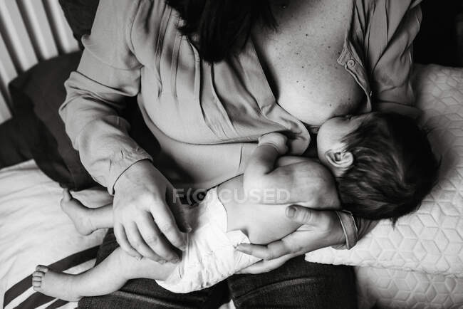 Von oben junge Mutter hält sich an Händen und stillt Neugeborenes in Decke gehüllt auf dem Bett zu Hause — Stockfoto
