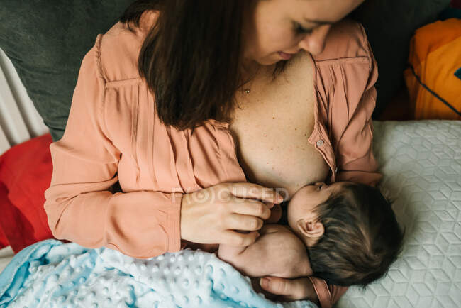 From above young mother holding on hands and breastfeeding newborn baby wrapped in blanket on bed at home — Stock Photo