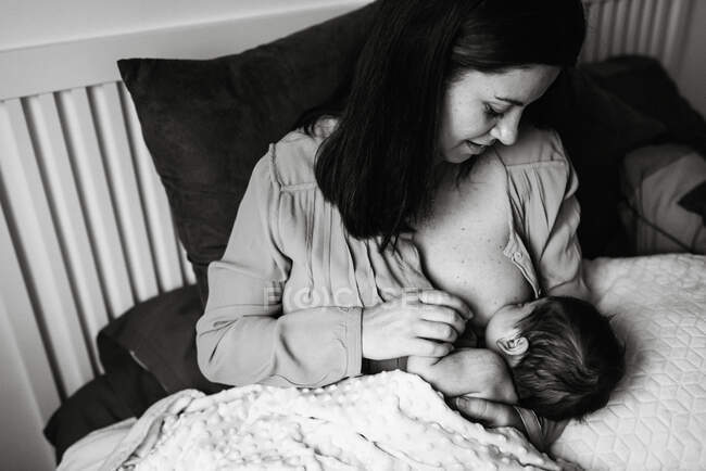 Dall'alto giovane madre che tiene le mani e allatta il bambino appena nato avvolto in una coperta sul letto a casa — Foto stock
