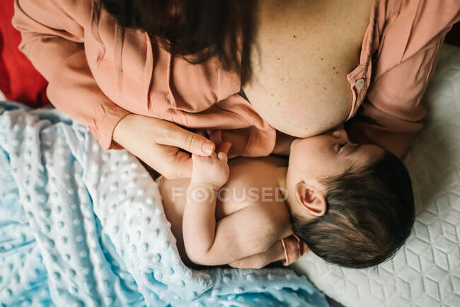 De cima mãe sem rosto segurando as mãos e amamentando bebê recém-nascido envolto em cobertor na cama em casa — Fotografia de Stock