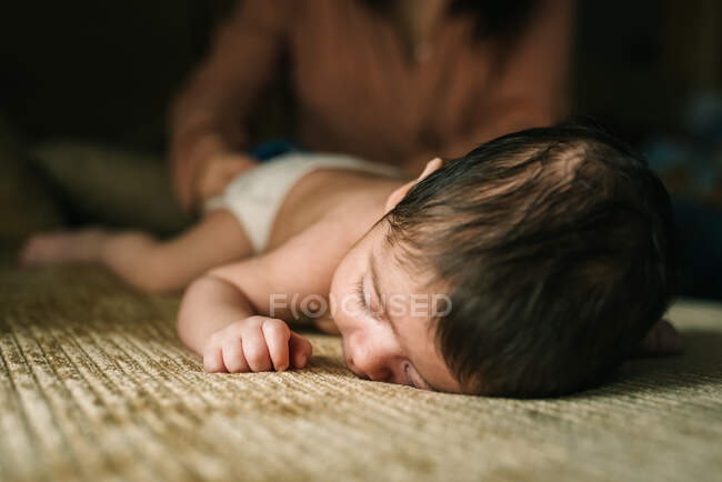 Cute little innocent newborn baby in back lying on sofa at home with mum behind — Stock Photo