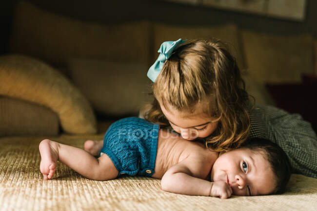 Симпатична маленька дівчинка цілує невинну новонароджену дитину в спині, лежить на дивані вдома — стокове фото