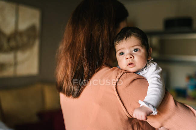 Rückseite unkenntlich brünette Mutter umarmt niedliches kleines Baby, das zu Hause wegschaut — Stockfoto