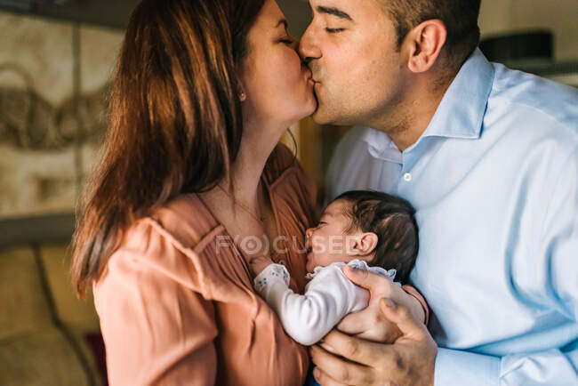 Щасливі батьки цілуються, тримаючи і обіймаючи плач дитини вдома — стокове фото