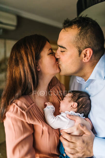 Счастливые родители целуются, держа и обнимая плачущего ребенка дома — стоковое фото