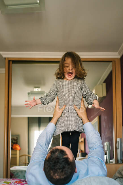 Faceless papà avendo divertimento con felice figlia holding su mani mentre sdraiato su letto — Foto stock