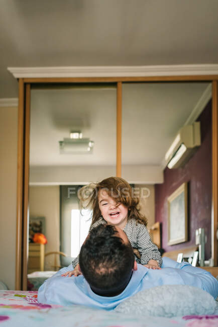 Papá sin rostro divirtiéndose con la hija feliz agarrándose de las manos mientras está acostado en la cama - foto de stock