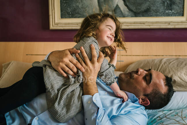 Papà avendo divertimento con felice figlia holding su mani mentre sdraiato su letto — Foto stock