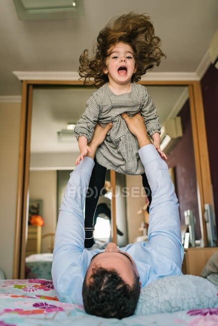 Faceless dad having fun with happy daughter holding on hands while lying on bed — Stock Photo