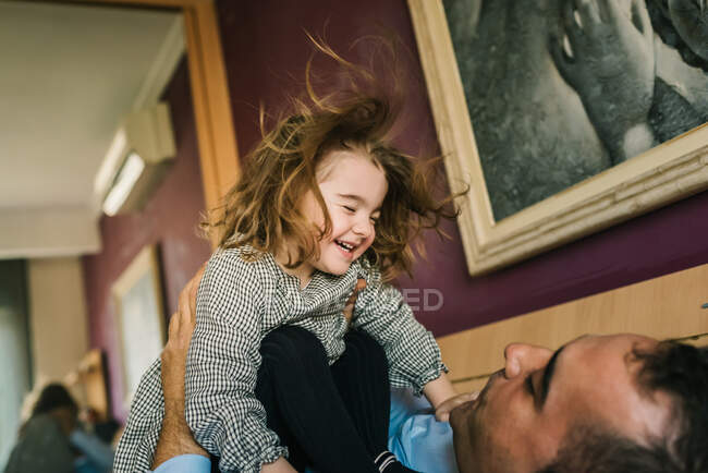 Papa s'amuser avec fille heureuse tenant sur les mains tout en étant couché sur le lit — Photo de stock