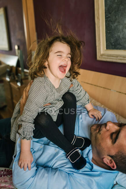 Dad having fun with happy daughter holding on hands while lying on bed — Stock Photo