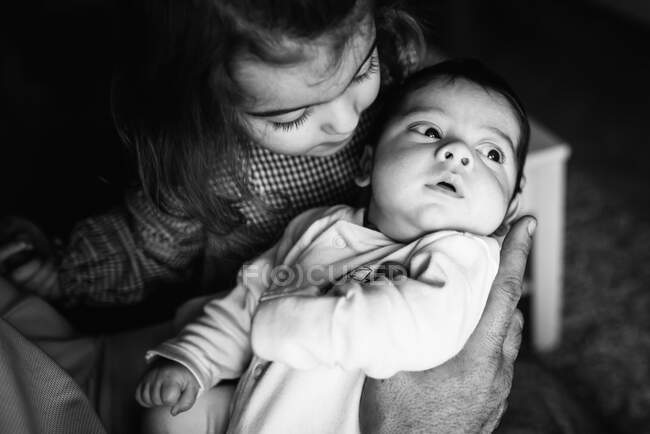 Brünette Schwester umarmt süßes kleines Baby, das zu Hause wegschaut — Stockfoto