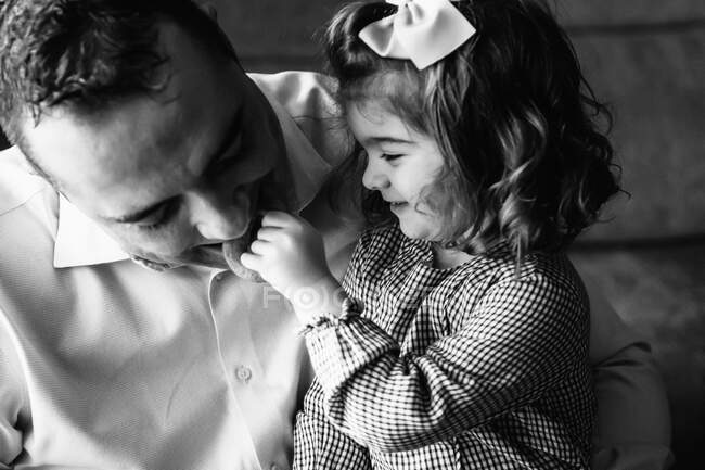 Батько обіймає милу маленьку дівчинку, дивлячись вбік і розважаючись вдома — стокове фото