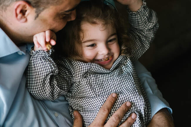 Батько обіймає милу маленьку дівчинку, дивлячись вбік і розважаючись вдома — стокове фото