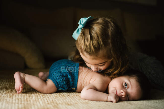 Soeur brune embrassant le dos du petit bébé regardant loin à la maison — Photo de stock