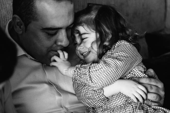 Père étreignant mignonne petite fille regardant loin et s'amusant à la maison — Photo de stock