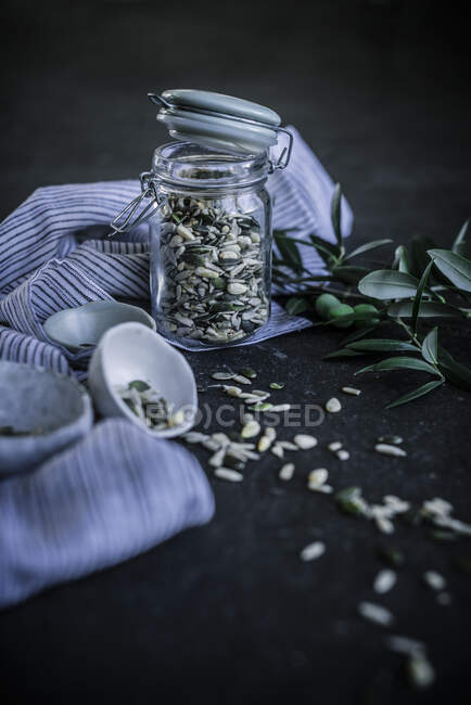 Banco di vetro con tappo con diversi semi stoffa e piastra con semi sparsi su tavolo scuro — Foto stock